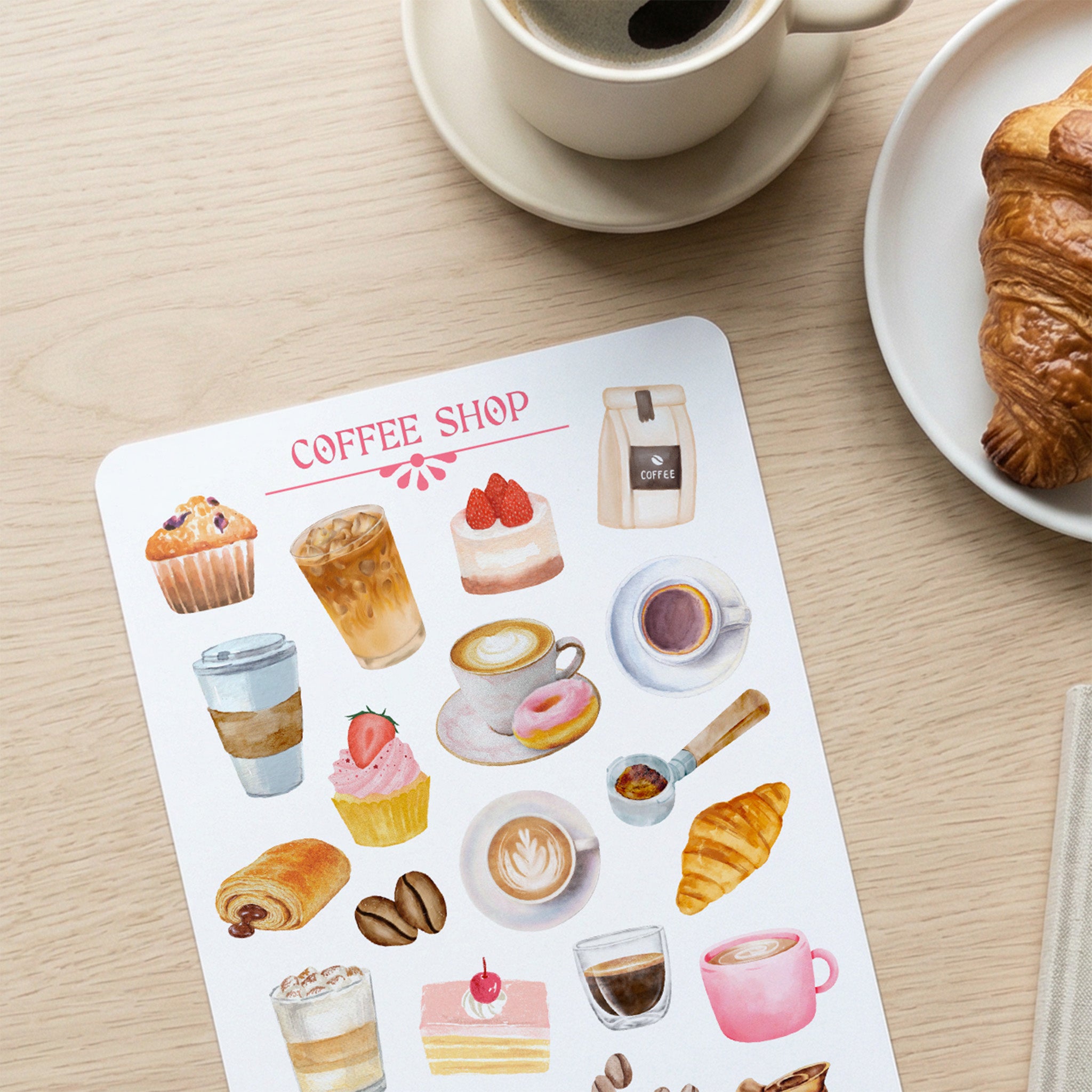 Sheet of coffee shop-themed stickers with a cup of coffee and croissant on a wooden table.