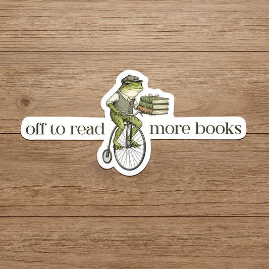 Frog on a bicycle with books, text 'off to read more books' on a wooden background