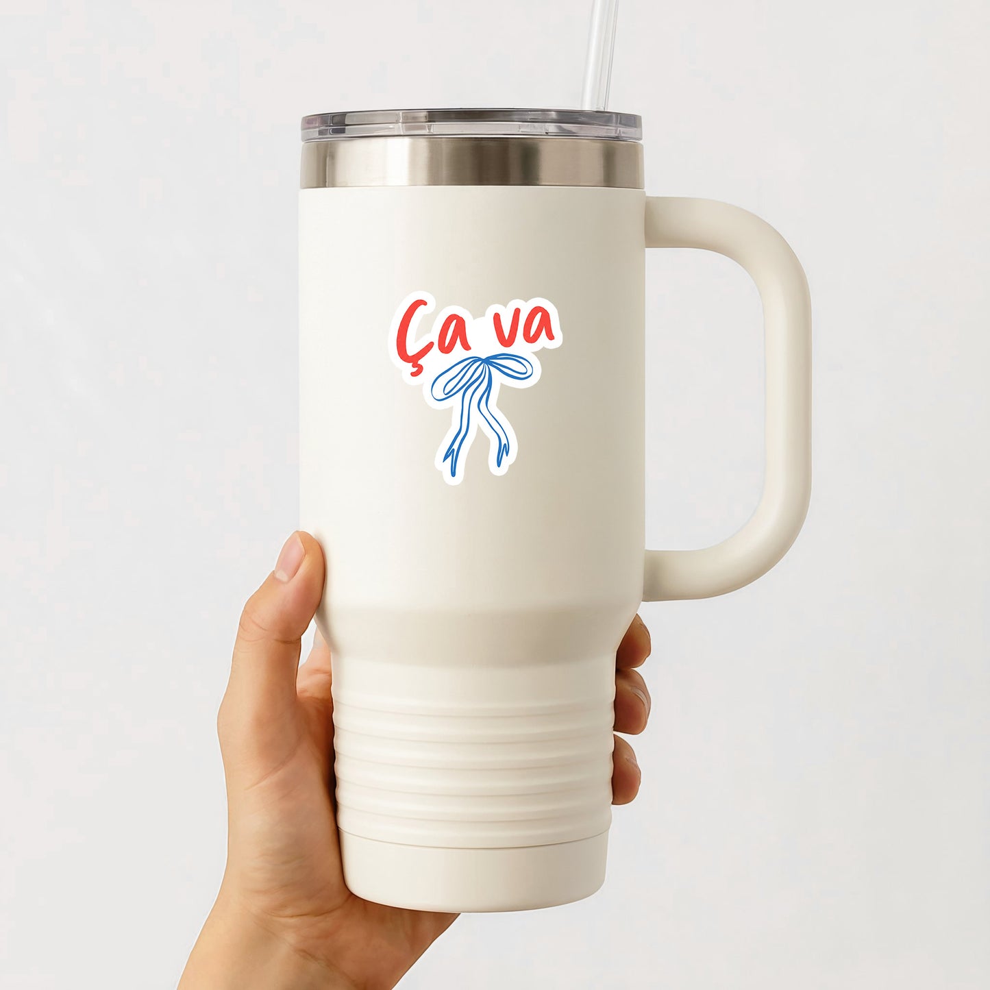 White insulated mug with 'Ca va' design held by a hand on a white background