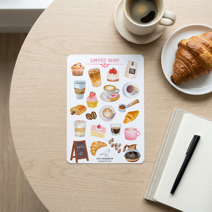 Sticker sheet with coffee shop-themed illustrations on a table with a cup of coffee and croissant.