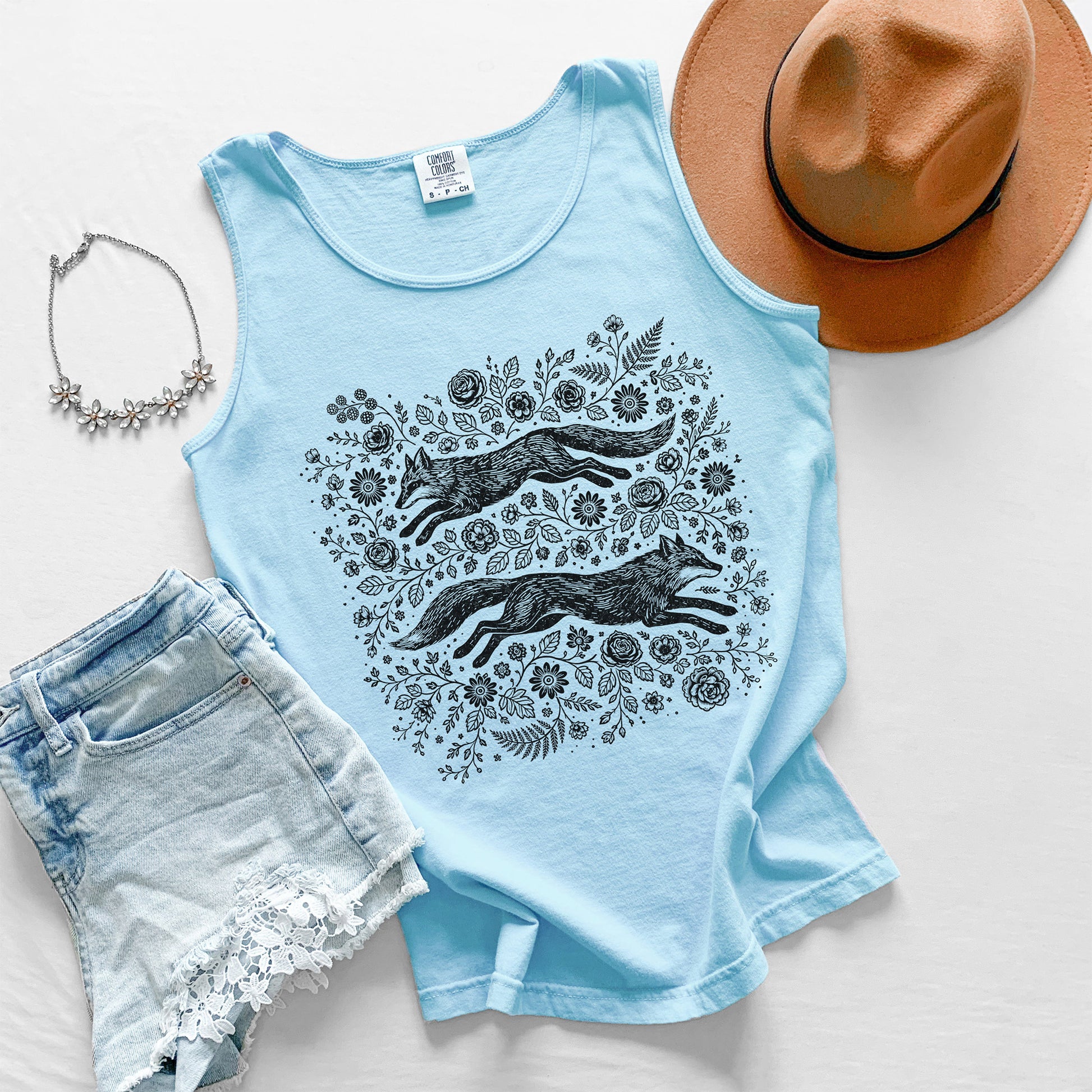 Light blue tank top with fox and floral design, paired with denim shorts, a hat, and necklace on a light background.