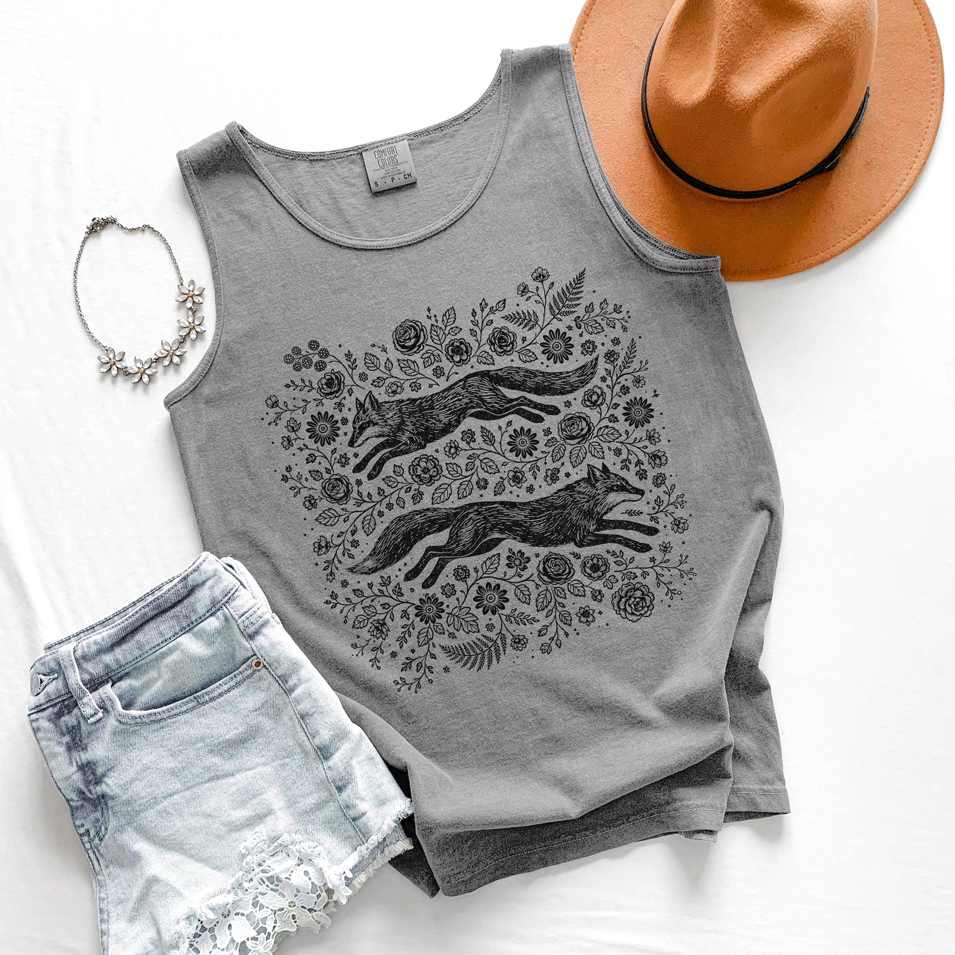 Gray tank top with fox and floral design, paired with denim shorts, a hat, and necklace on a white background.