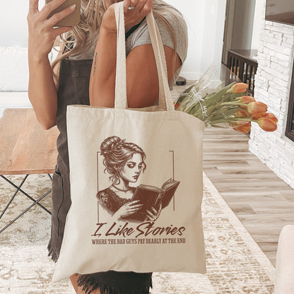 Person holding a tote bag with a design of a woman reading a book and the text I Like Stories standing in a light colored living room