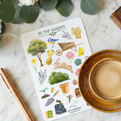 Sticker sheet titled 'In the Garden' with gardening-themed illustrations on a marble surface with a cup of coffee and pen.