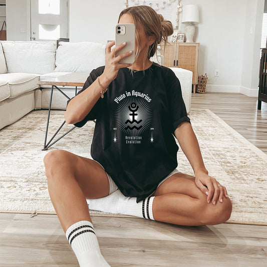 Woman sitting on a rug in a living room wearing a black t-shirt with an astrological design and text.