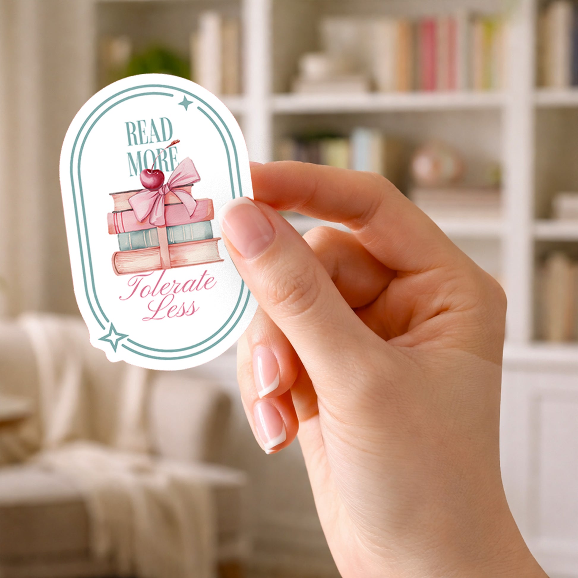 Hand holding a sticker with book-themed design and text that says Read More Tolerate Less  with a stack of books tied with a bow