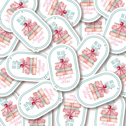 A pile of stickers with book-themed design and text that says Read More Tolerate Less  with a stack of books tied with a bow