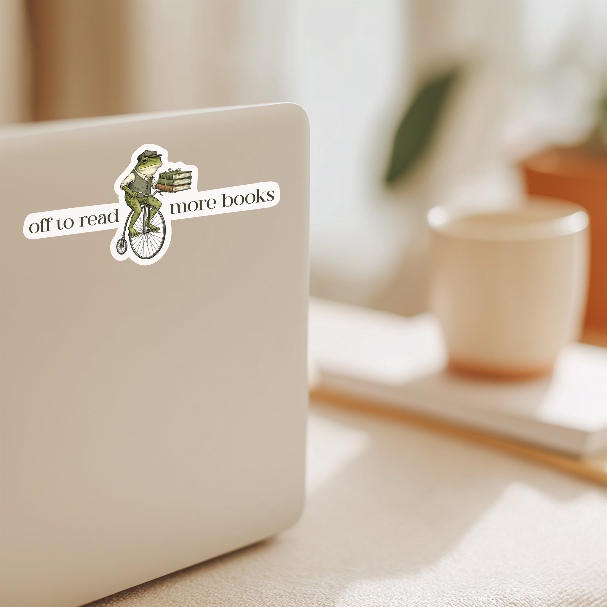 Laptop with a sticker featuring a frog with text that says off to read more books on a computer on a desk with a blurred background