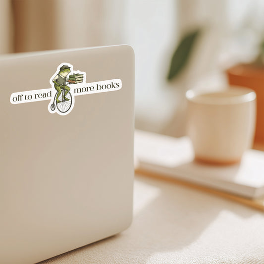 Laptop with a sticker featuring a frog with text that says off to read more books on a computer on a desk with a blurred background