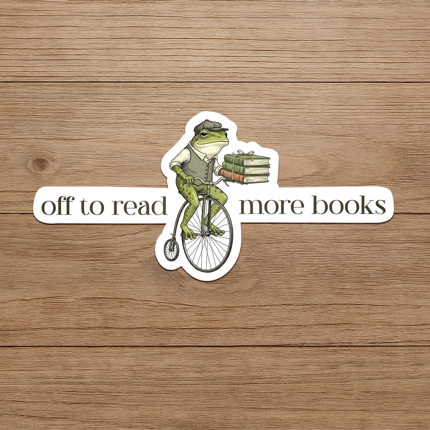 Frog on a bicycle with books, text 'off to read more books' on a wooden background