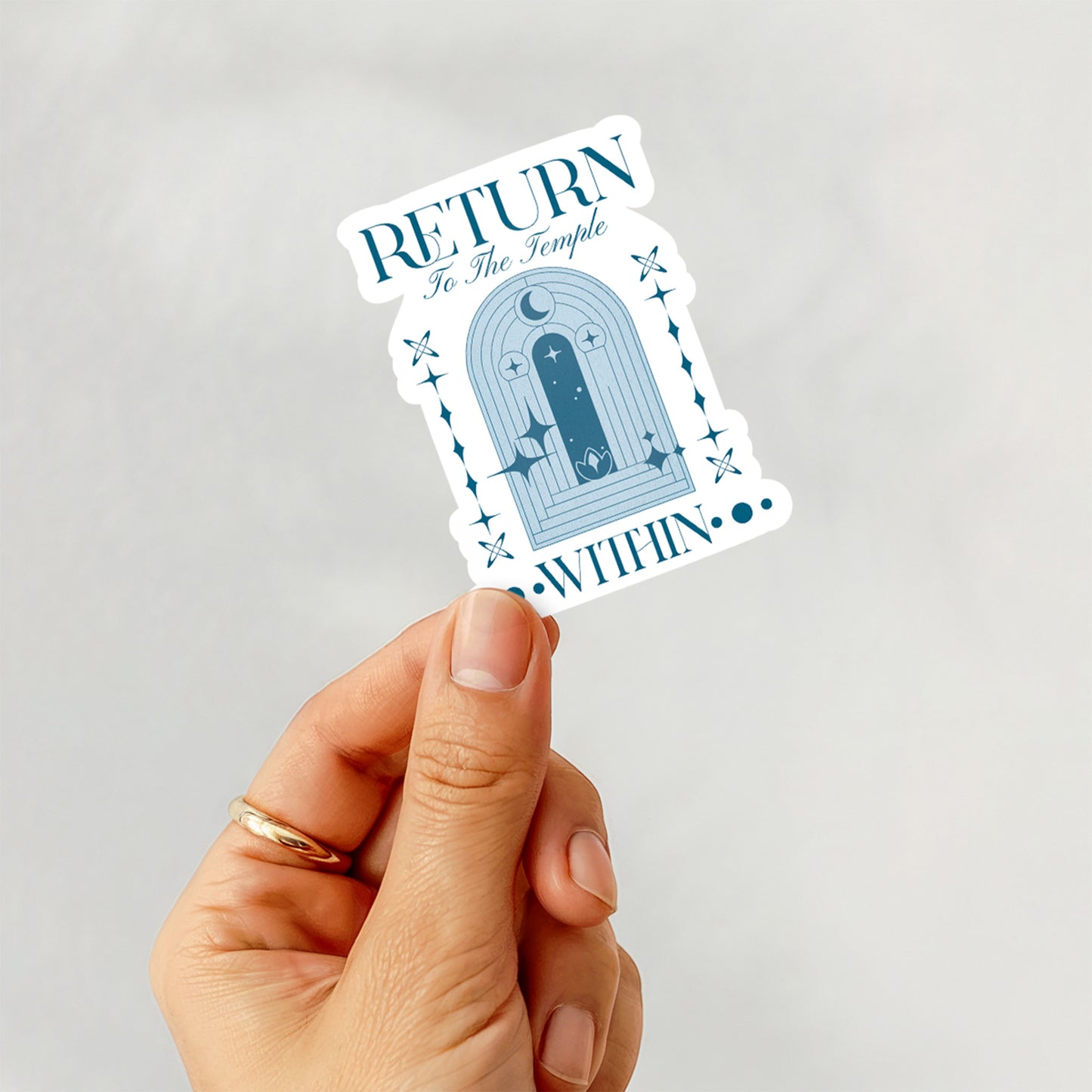 Hand holding a sticker with a temple design and text on a light gray background