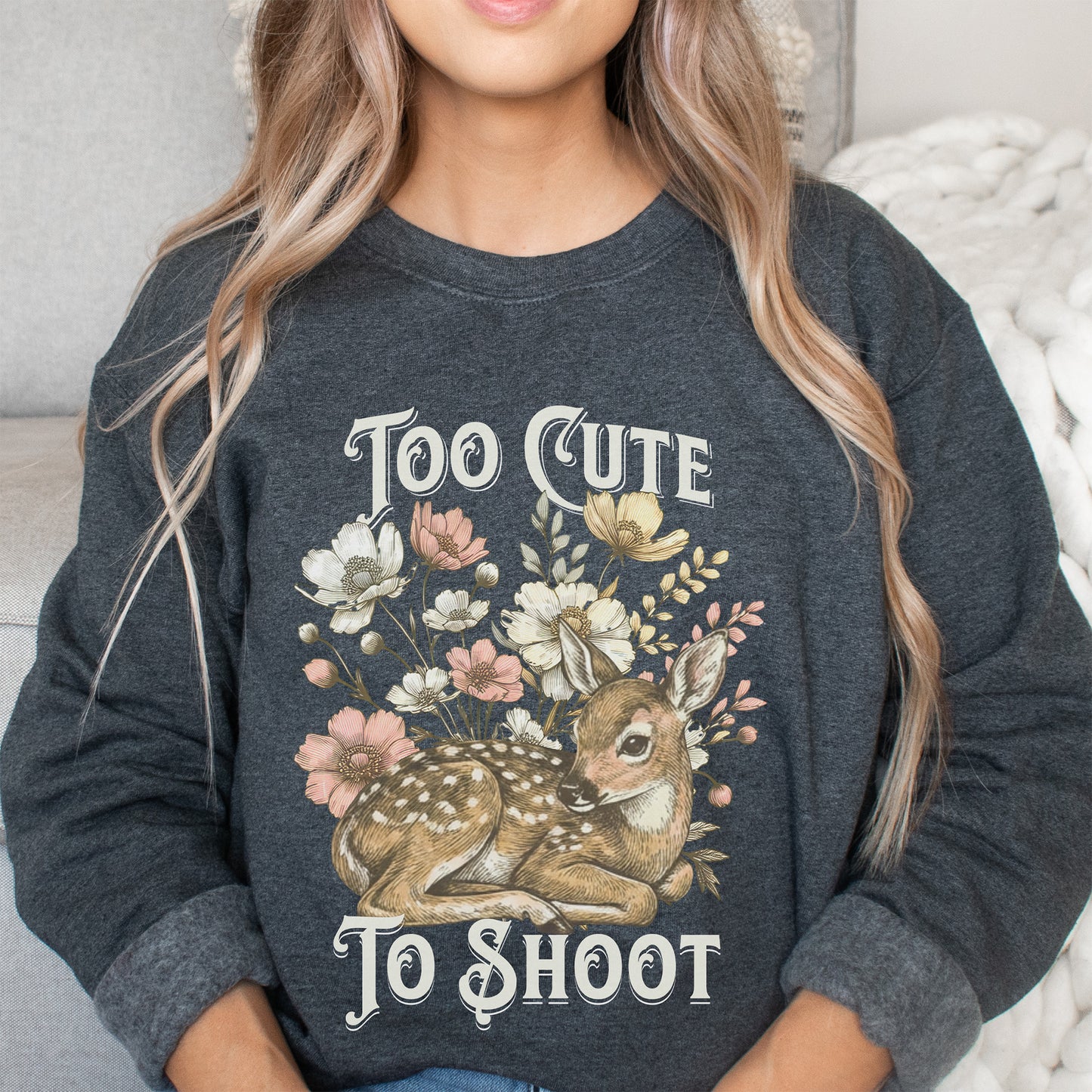Person wearing a dark gray sweatshirt with a deer and floral design and text 'Too Cute To Shoot'.
