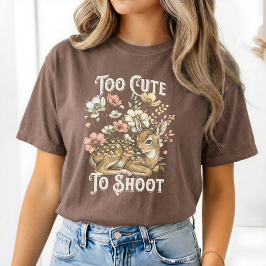 Woman wearing a brown short sleeved t-shirt with a deer and floral design and text reading too cute to shoot.