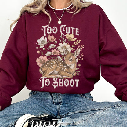 Maroon sweatshirt with a deer and floral design and text 'Too Cute To Shoot' worn by a woman in denim jeans.