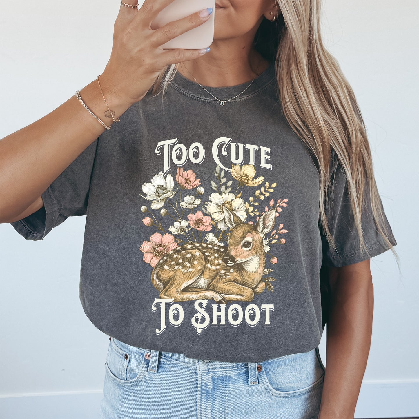 Woman wearing a t-shirt with a deer and floral design and text 'Too Cute To Shoot'.