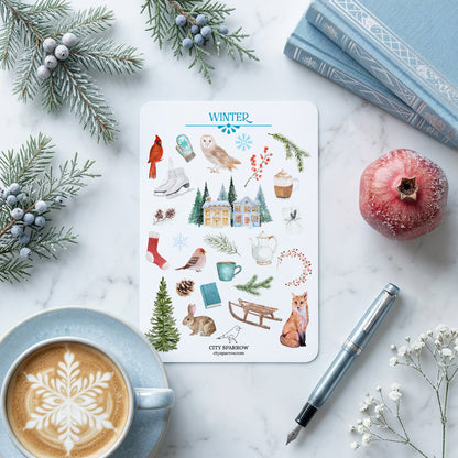 Sheet of winter-themed stickers on a marble surface with a cup of coffee, pen, and decorative elements.