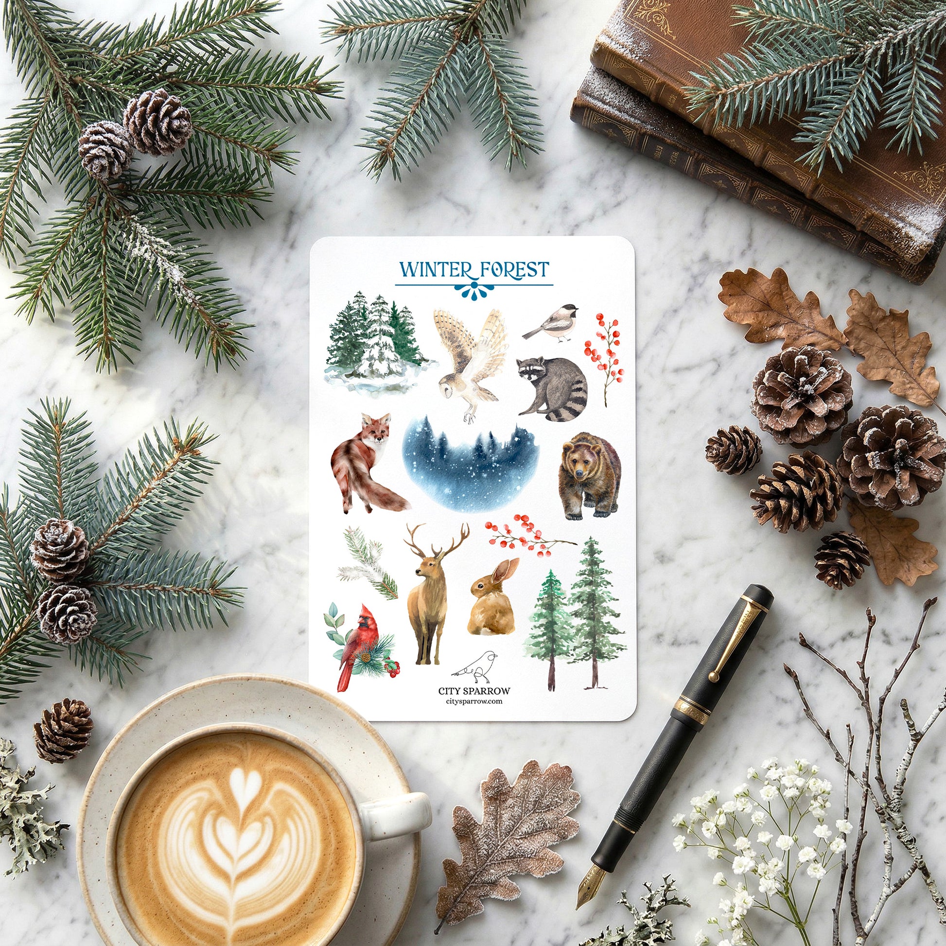 Sheet of winter-themed stickers with nature illustrations on a marble surface with a cup of coffee, pen, and decorative elements.
