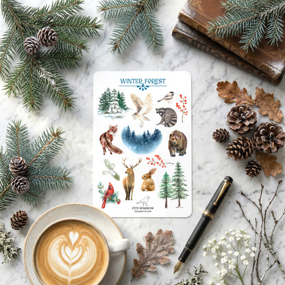 Sheet of winter-themed stickers with nature illustrations on a marble surface with a cup of coffee, pen, and decorative elements.